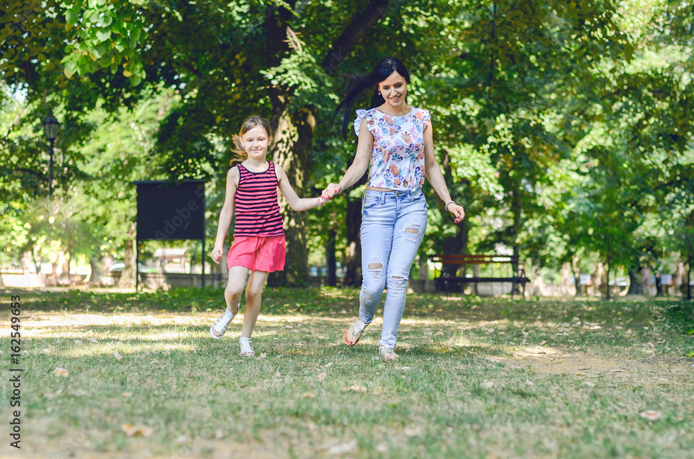 Fototapeta premium Beautiful young modern mom and her daughter walking through the park
