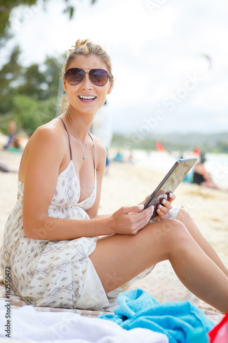 Happy and smile Relaxed young brunette woman in sunglasses with tablet pc computer on the beach. Looking to camera
