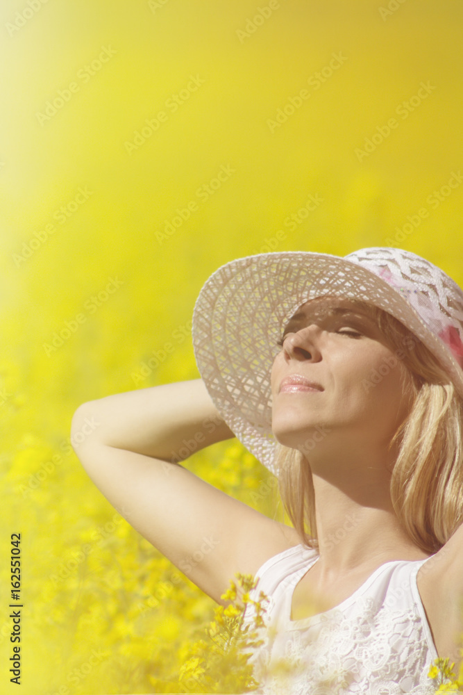 Fototapeta premium Young woman with a hat enjoying summer on the rape field.