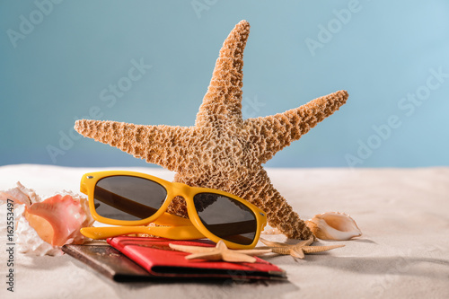 Composition with starfish, sunglasses, passports and shells on sand against color background. Concept of travel and vacation © Africa Studio
