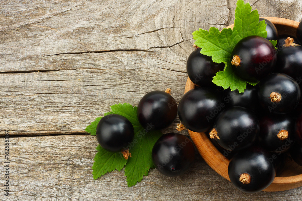 black currant in wooden bowl with green leaf on old wooden background. top view black currant in wooden bowl with green leaf on old wooden background. top view