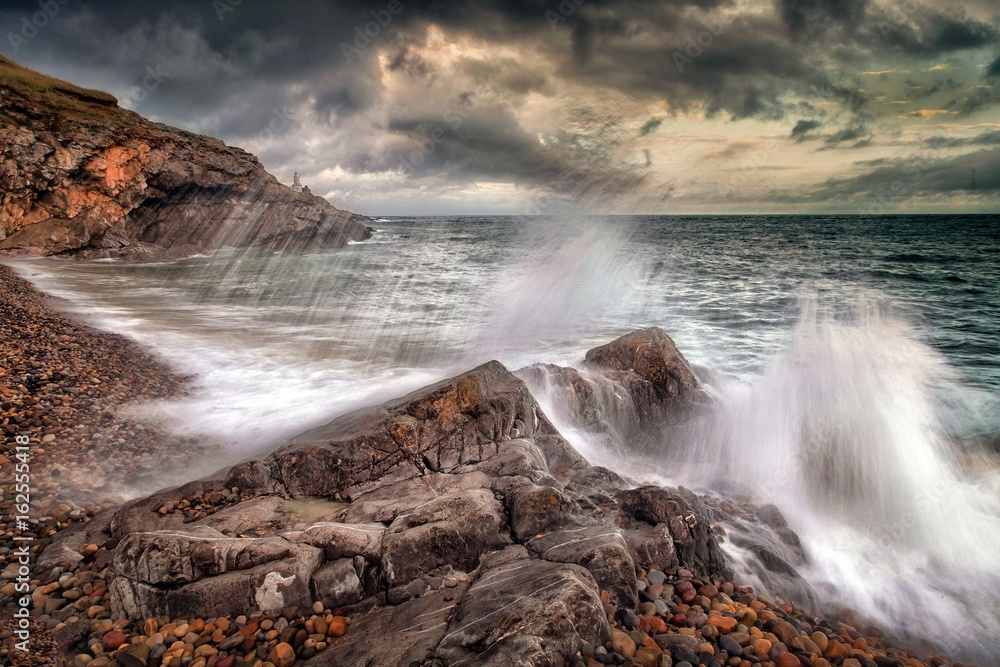 Obraz premium Slow shutter speed showing the movement of a wave crashing on Bracelet Bay on the Gower peninsula, Swansea, South Wales.