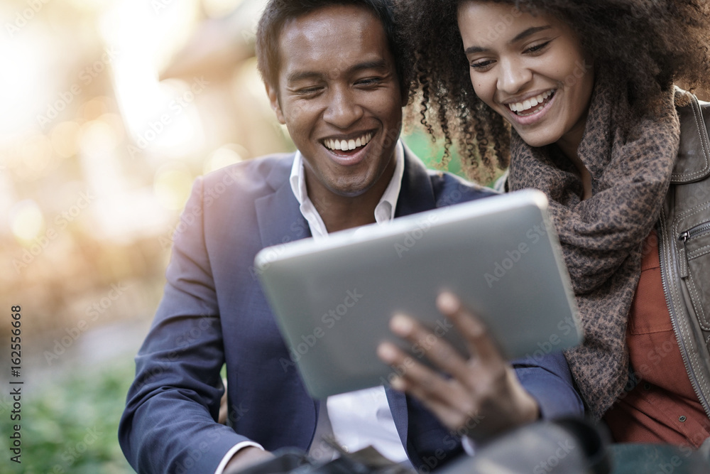 Couple sitting in park connected on digital tablet Couple sitting in park connected on digital tablet