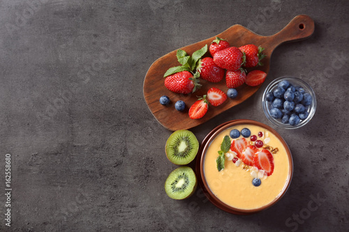 Bowl of fresh yogurt smoothie with fruits on grunge background