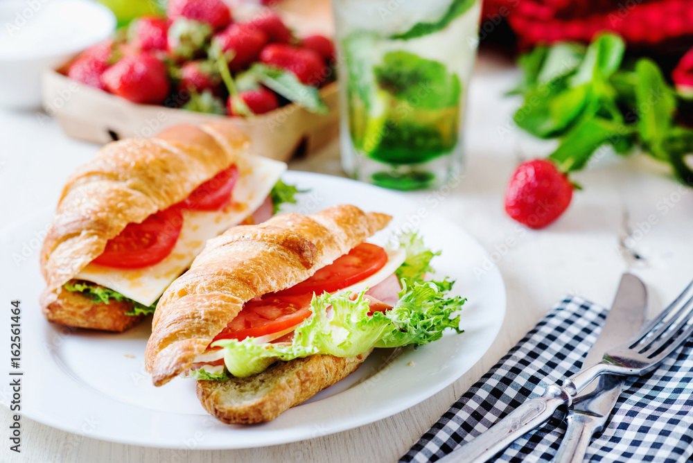Breakfast, business lunch, sandwiches croissant with ham, cheese, sauce, lettuce, tomato and strawberry mint ice-cold cocktail on a light background Breakfast, business lunch, sandwiches croissant with ham, cheese, sauce, lettuce, tomato and strawberry mint ice-cold cocktail on a light background