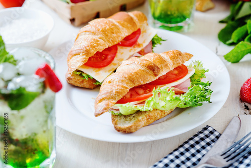 Breakfast, business lunch, sandwiches croissant with ham, cheese, sauce, lettuce, tomato and strawberry mint ice-cold cocktail on a light background 