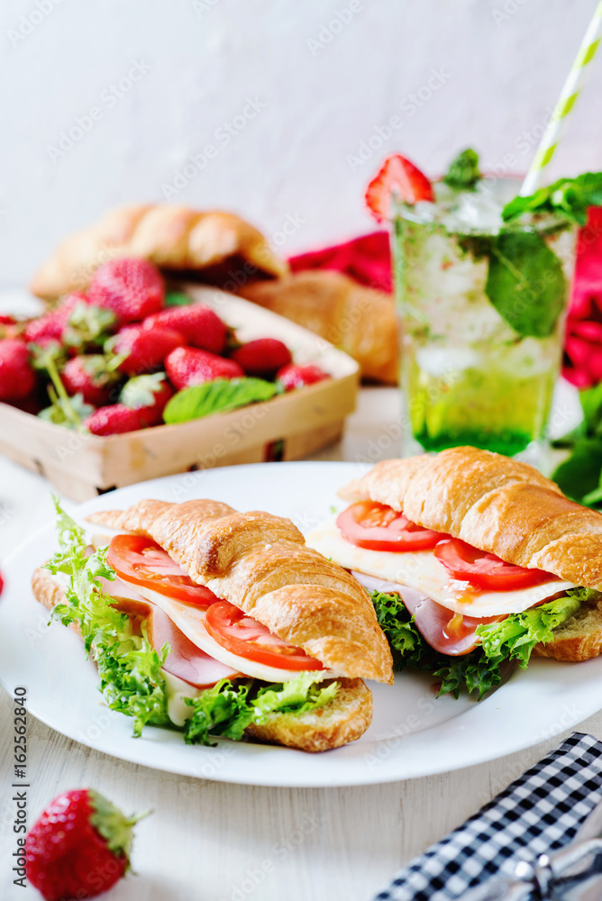 Breakfast, business lunch, sandwiches croissant with ham, cheese, sauce, lettuce, tomato and strawberry mint ice-cold cocktail on a light background 