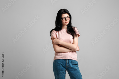 Portrait of smart beautiful brunette girl in eyeglasses with natural make-up, on grey background.