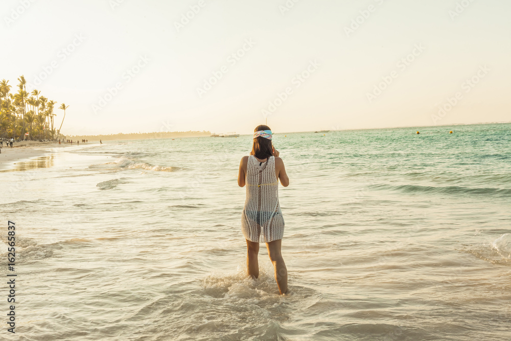 Rear view woman walking in the seashore. Tropical caribbean beach. Sunset Rear view woman walking in the seashore. Tropical caribbean beach. Sunset