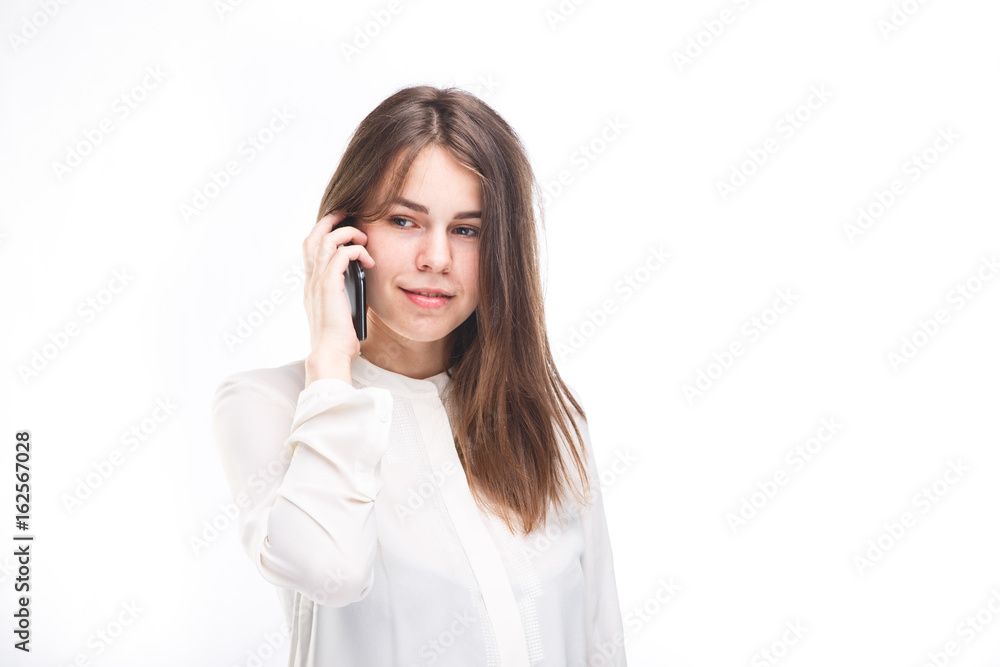Beautiful young girl in a white shirt on white isolated background talking on a mobile phone. Smiles, portrait to the waist Beautiful young girl in a white shirt on white isolated background talking on a mobile phone. Smiles, portrait to the waist
