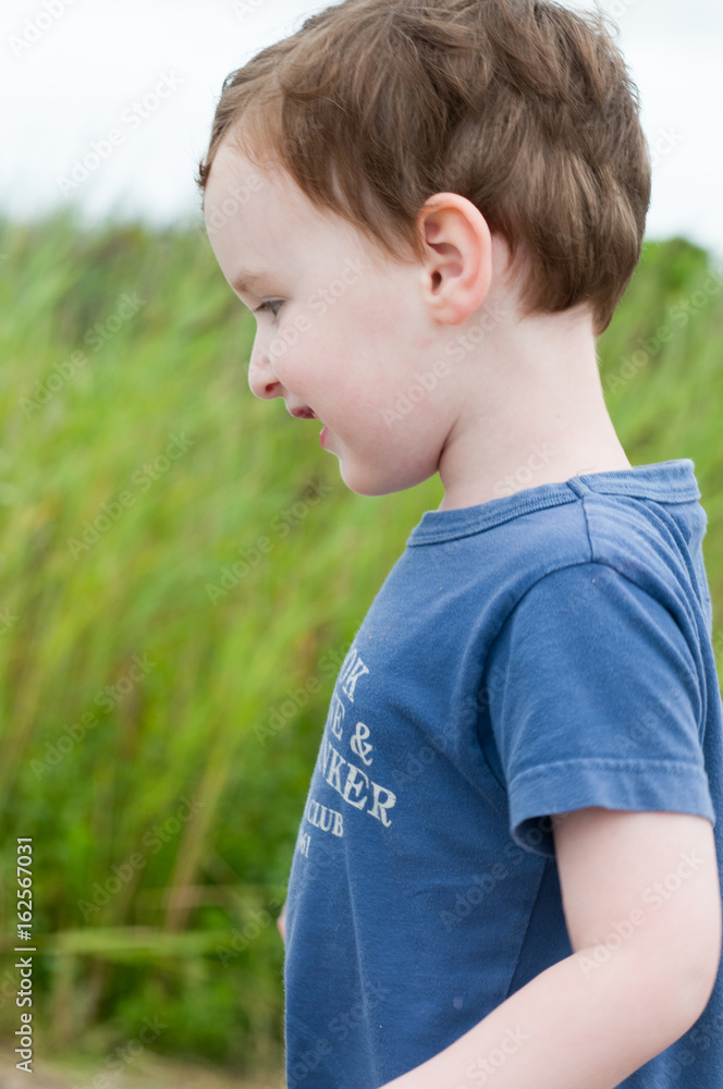 Profile of young boy walking outside along beach sand dunes with reeds Profile of young boy walking outside along beach sand dunes with reeds