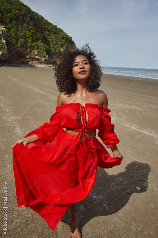 Female dark skin model with curly hair in red dress enjoing at the sea  coast Stock-Foto | Adobe Stock