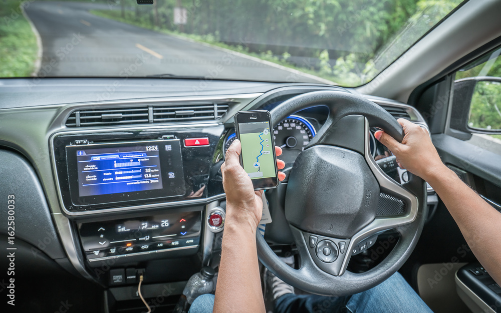 Hand Holding Steering Wheel And Watching GPS On Mobile Smartphone