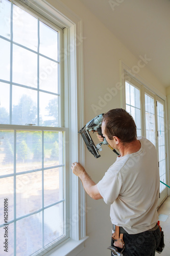 Carpenter brad using nail gun to moldings on windows, framing trim,
