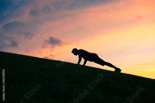 Silhouette of man doing push up outdoors.  photo