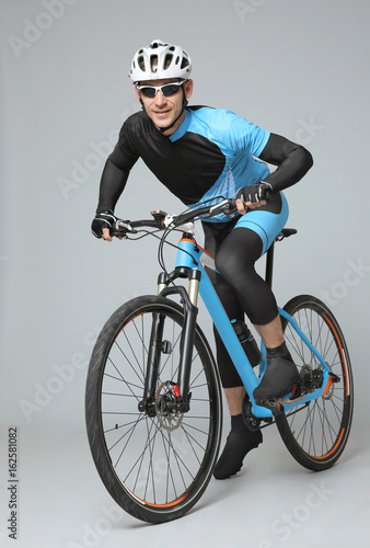 Fototapeta Naklejka Na Ścianę i Meble -  Young sporty cyclist riding bicycle on grey background