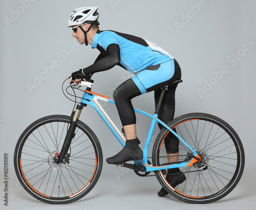 Fototapeta Naklejka Na Ścianę i Meble -  Young sporty cyclist riding bicycle on grey background