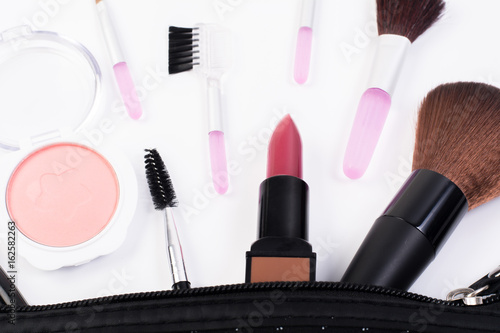 Top view of a make up bag, with cosmetic beauty products spilling out onto a white background.