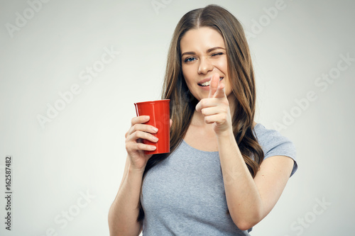Funny girl holding red coffee cup pointing finger at camera.