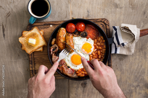 Man is eating English breakfast on wooden light table photo