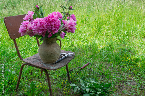 Peony flowers in a  clay  jug on old vintage chair in the garden photo