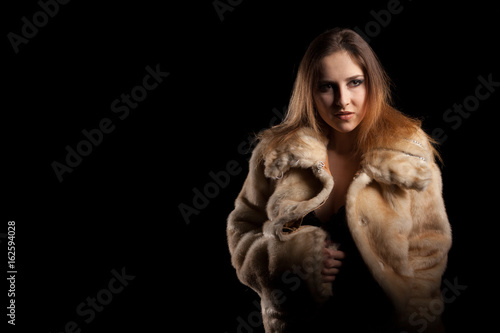 Hot sexy woman in fur and bra on black background in studio photo. Erotic attractive model