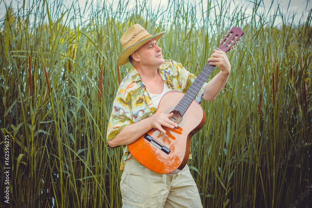 Φωτογραφία Funny older man in print shirt tourist playing guitar and sing song on nature ou