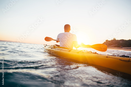 Man kayaker paddling kayak at sunset photo