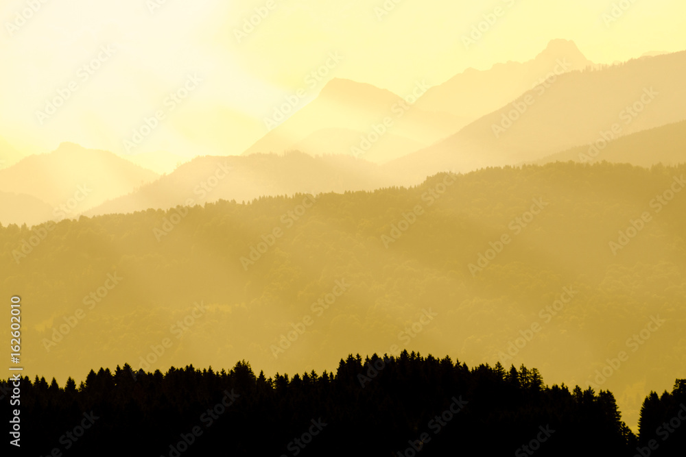 Spectacular view of mountain silhouettes. Yellow sunlight and sunbeams.