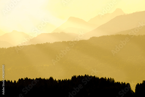 Spectacular view of mountain silhouettes. Yellow sunlight and sunbeams.