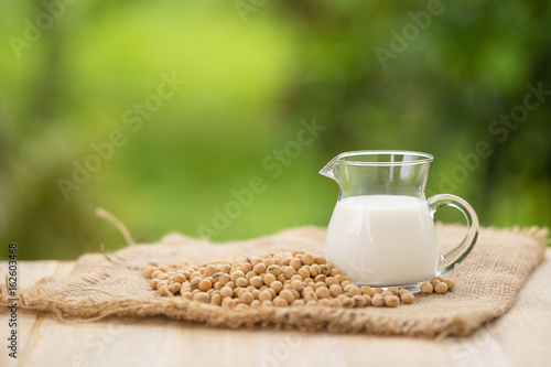 Soy milk and soy beans in wooden cup with abstract blurred forest nature background.