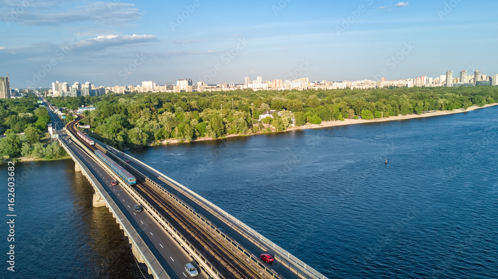 Aerial top view of Metro railway bridge with train and Dnieper river from above, skyline of city of Kiev, Ukraine
