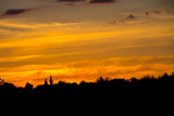 Orange sunset over silhouettes of village and trees