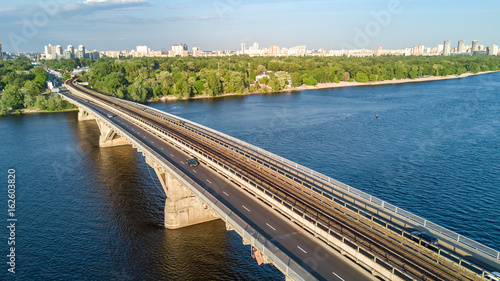 Aerial top view of Metro railway bridge with train and Dnieper river from above  skyline of city of Kiev  Ukraine  