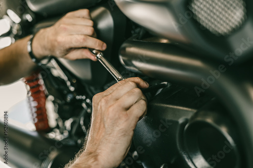Closeup image of motorcycle mechanic repairing motorcycle in automobile store. Man hands with special tools.