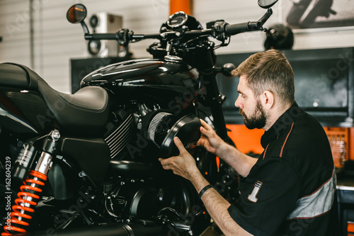 Professional mechanic change the air filter in the motorcycle. Handsome young man repairing motorcycle in repair shop.