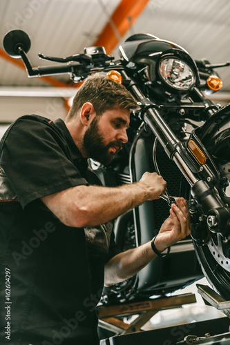 A professional mechanic unscrews the front wheel of a motorcycle. Bike is on the lift at the service station.