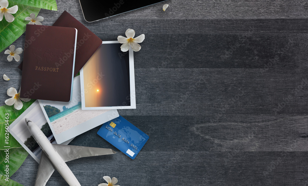 Top view of travel accessories, Passport, Credit card, Seascape photos,Airplane, Smartphone, Laptop, Sneakers and Plumeria flower on grey wooden background.