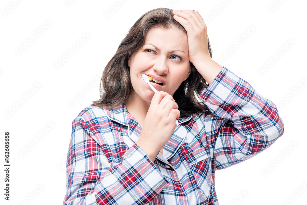 Unsatisfied woman brushing her teeth in the morning in pajamas on white background Unsatisfied woman brushing her teeth in the morning in pajamas on white background