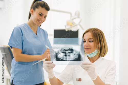 woman dentist with her assistant examine dental x-ray photo