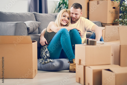 Couple sitting on a floor in new apartment, boxes all around © chika_milan