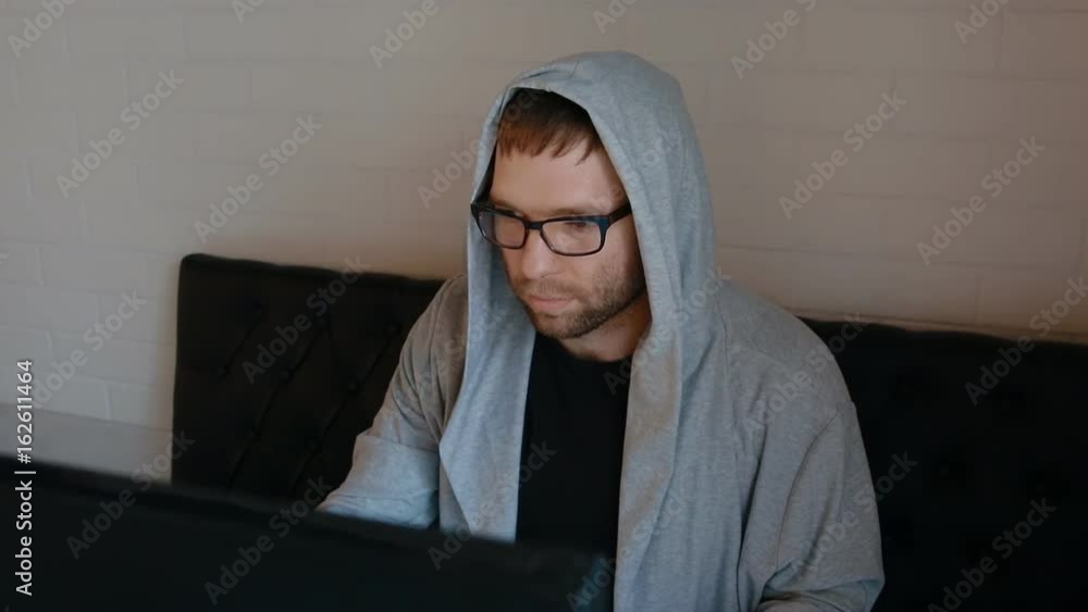 Young man in hood play video game sitting behind big monitor. His eyes browse the monitor. Young man in hood play video game sitting behind big monitor. His eyes browse the monitor.