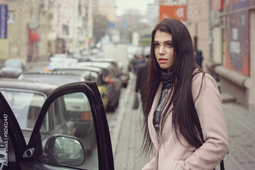 Girl gets into the car. She is dressed in a coat © alexshalamov