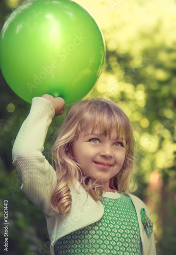 Portrait of a beautiful little blonde girl with green balloon in the park at the sunny summer day.