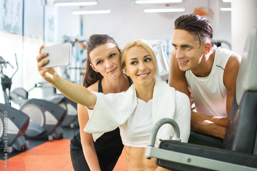 Group of happy young people taking selfie by smartphone in gym. Group of happy young people taking selfie by smartphone in gym.
