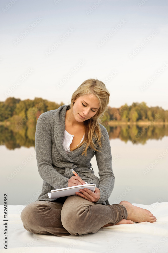 Young woman writing,sketching, by lake