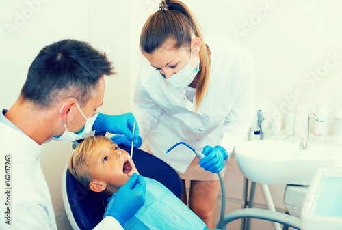 Stomatologist man with woman assistant are diagnosticating to young patient which is sitting