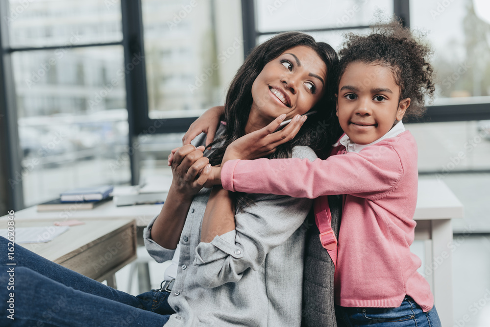 daughter hugging mother that talking on smartphone at workplace, work and life balance concept daughter hugging mother that talking on smartphone at workplace, work and life balance concept