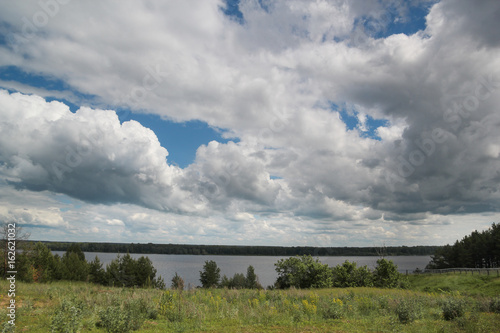 Field by a river on the background of a sky with big clouds heap