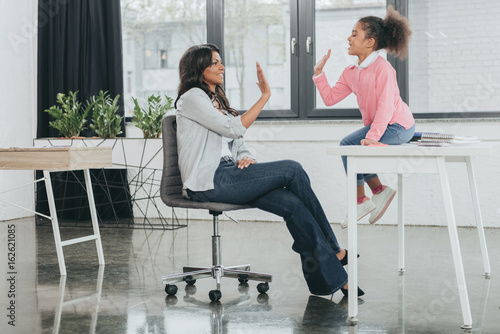 side view of mother giving high five to daughter in business office, work and life balance concept